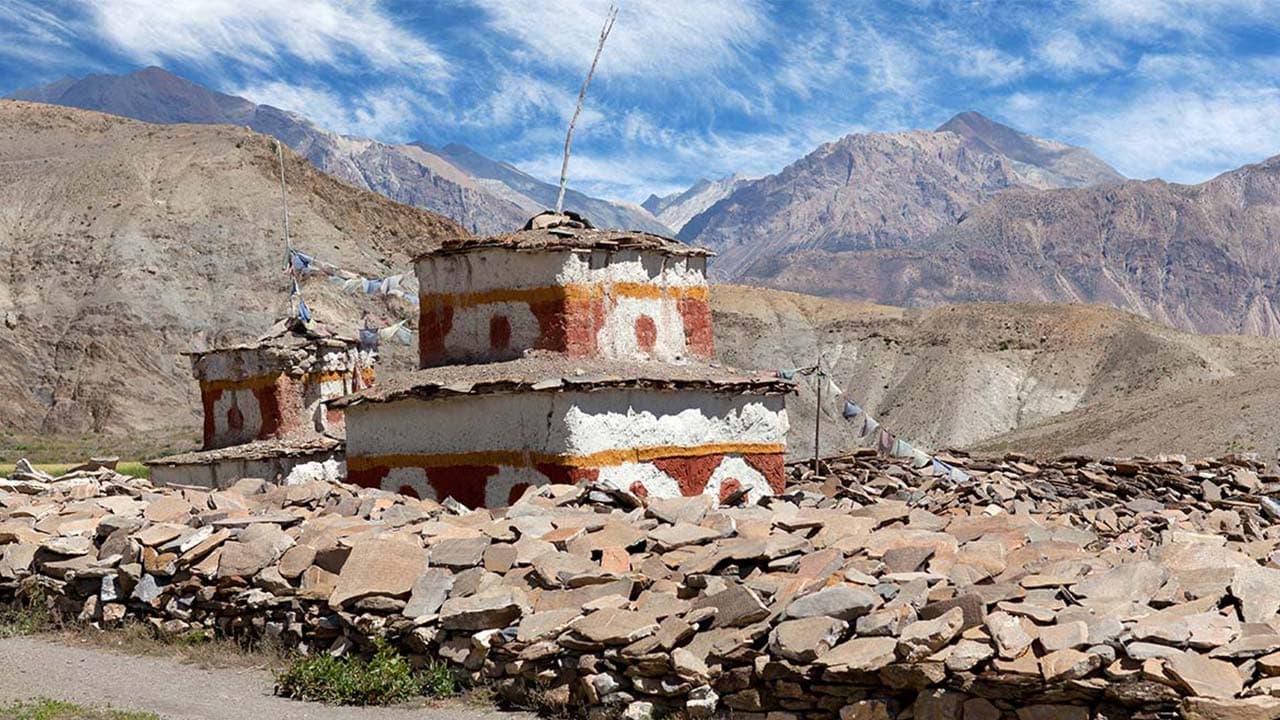 Whitewashed chortens with red bands and prayer flags surrounded by stone walls and dry mountain slopes on the Upper Dolpo Trek.
