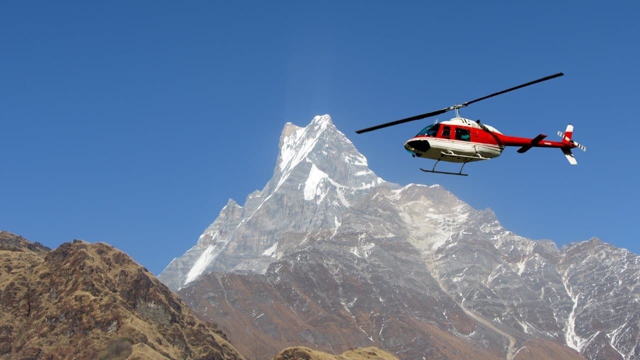Red and white helicopter flying in front of Machhapuchhre peak.