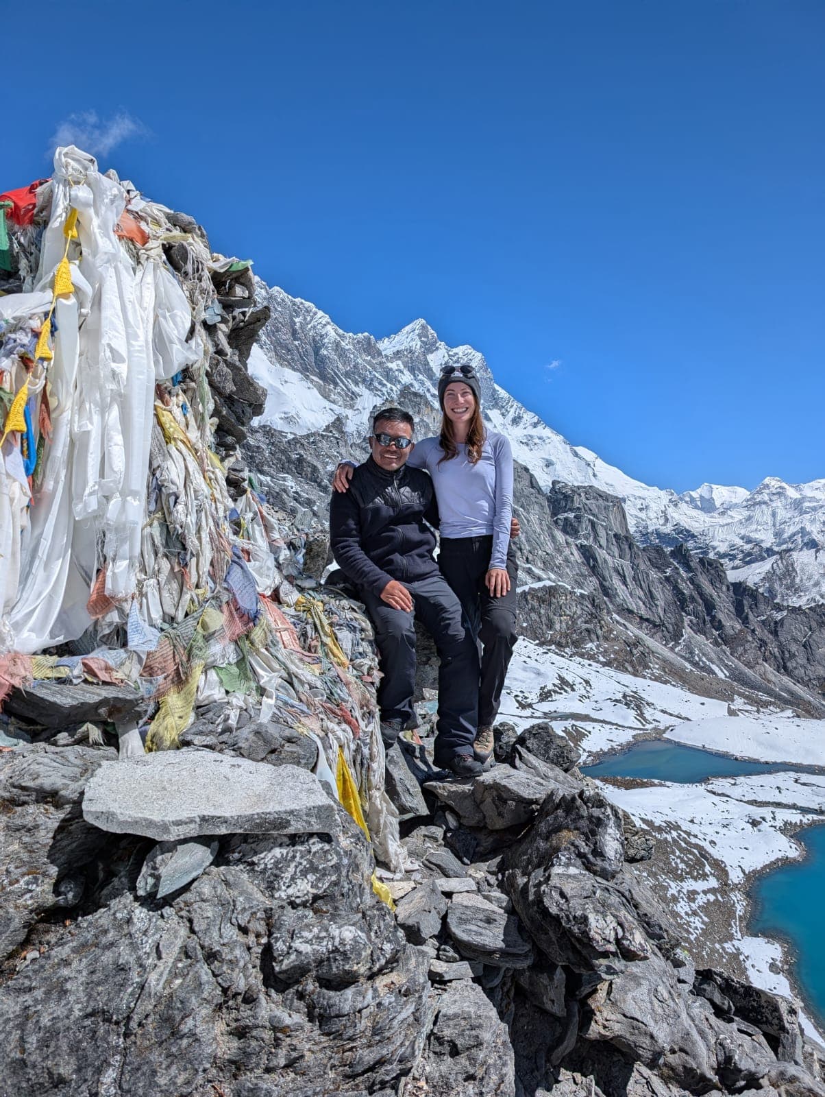 rekkers by prayer flags on Gokyo Ri overlooking turquoise lakes.