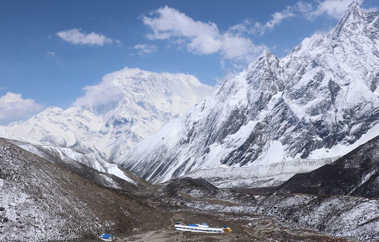 Small teahouses sit nestled in a rugged Himalayan valley below towering snow-covered peaks and glaciers on the Manaslu route.