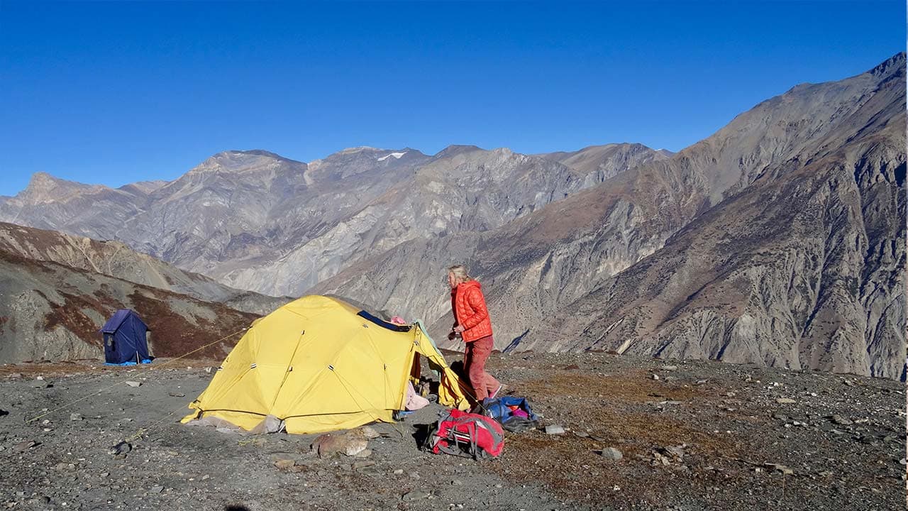 Yellow camping tent and trekker in arid mountain terrain on the Upper Dolpo Trek.