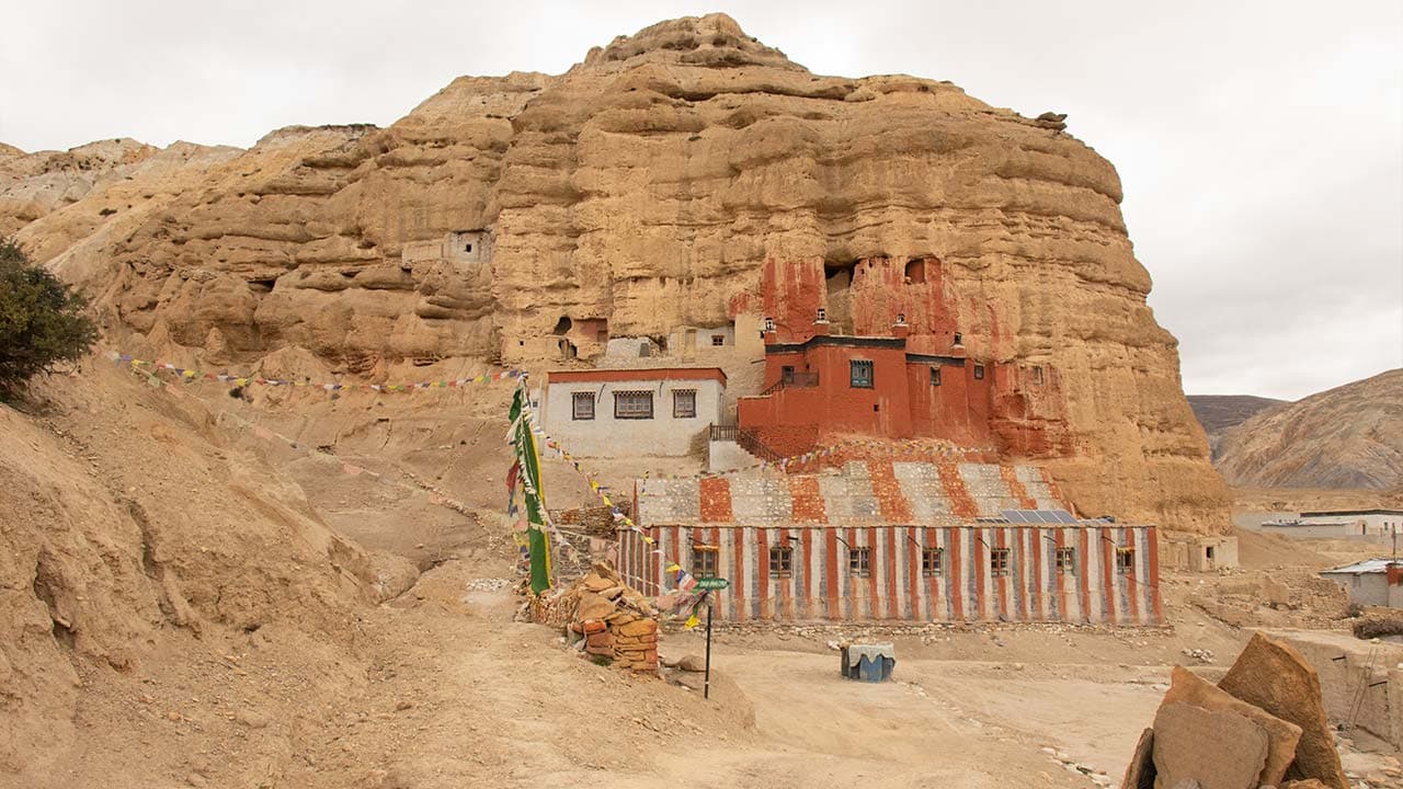 Ancient red and white Lo Gekar Monastery built into dramatic desert canyons during the 13 Days Upper Mustang Trek.