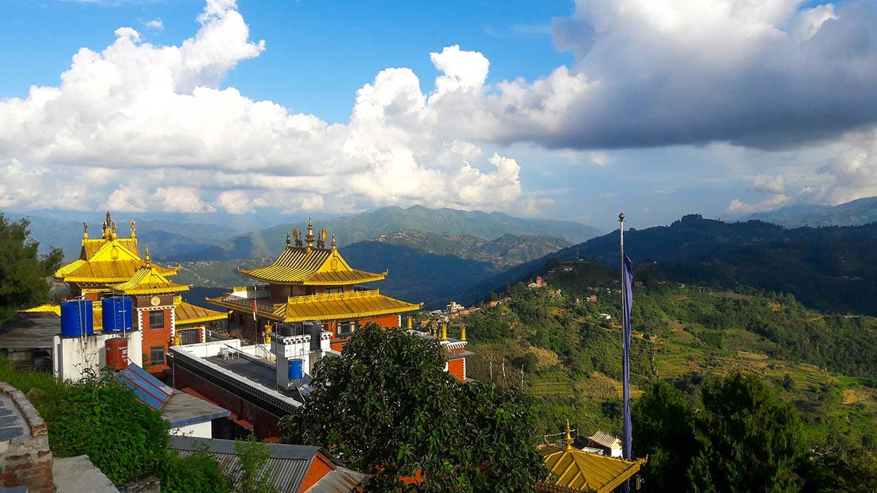 Ornate golden temple roofs, blue skies, and rolling hills at the sacred Namobuddha monastery.