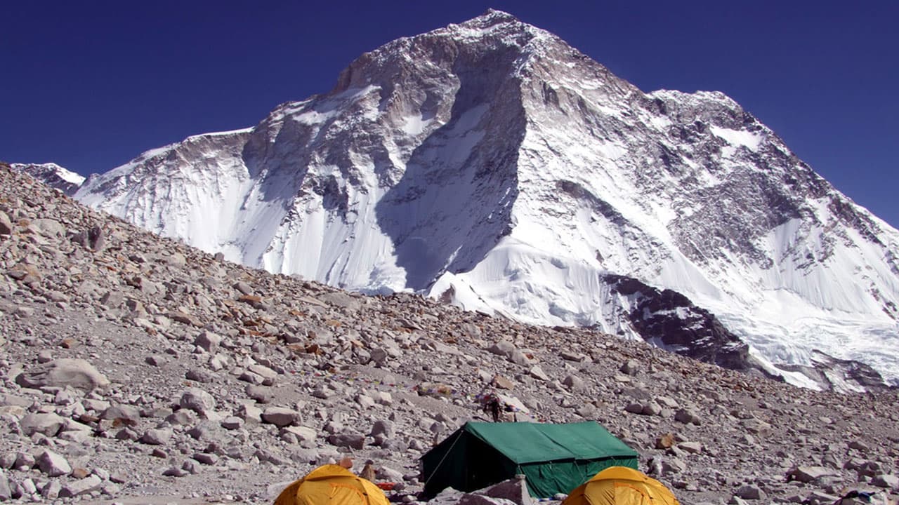 Expedition tents pitched on rocky moraine beneath towering granite walls.