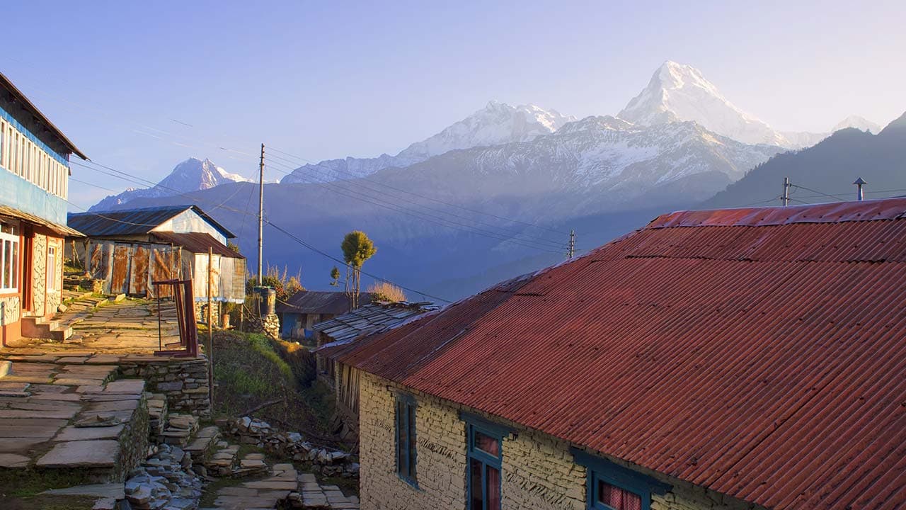 Stone-paved village path in Ghorepani lined with red-roofed lodges and snow-capped Annapurna peaks in the background.