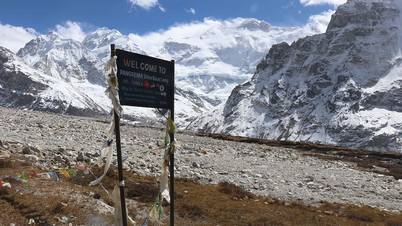 Signpost at Pangpema view base camp with snowy mountain peaks and glacier in the background.