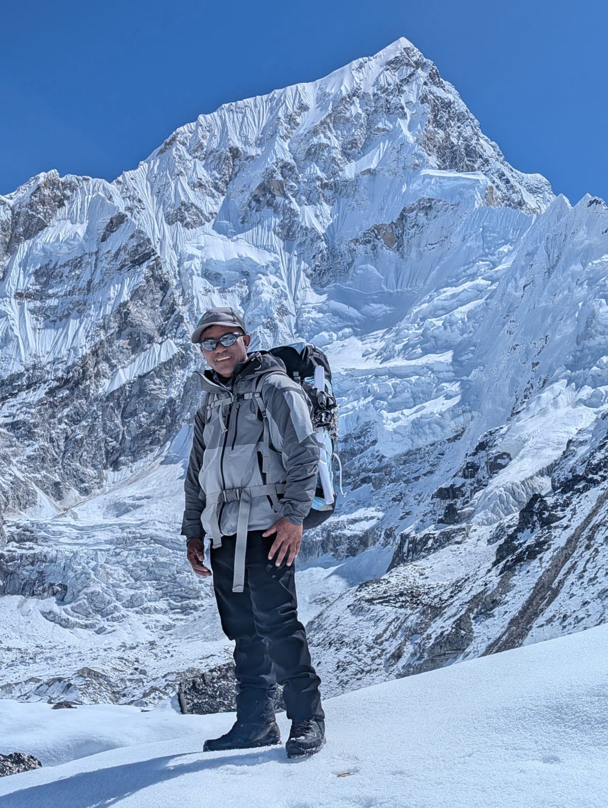 A trekker standing on a snowy mountain ridge in front of a towering peak.