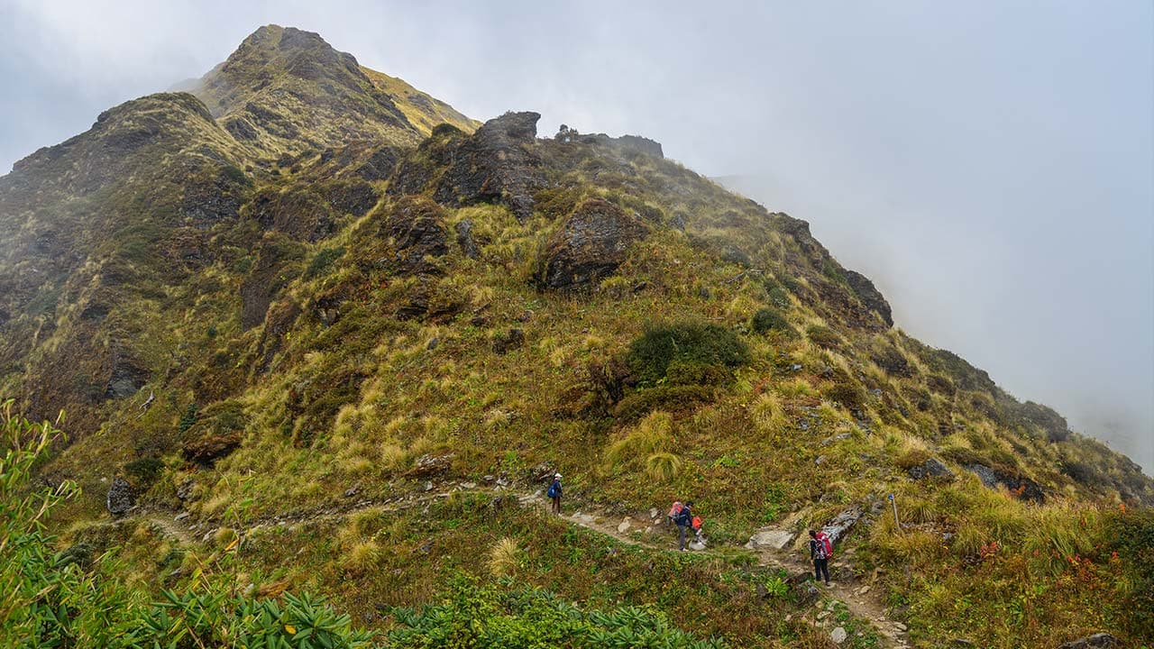 Trekkers hiking a narrow hill path during the Khopra Danda trek in Nepal's Annapurna region.