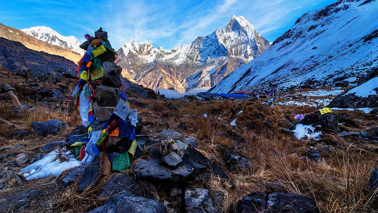Stone cairn with colorful prayer flags in the foreground overlooking snow-capped Machhapuchhre mountain on the Annapurna Base Camp trail.
