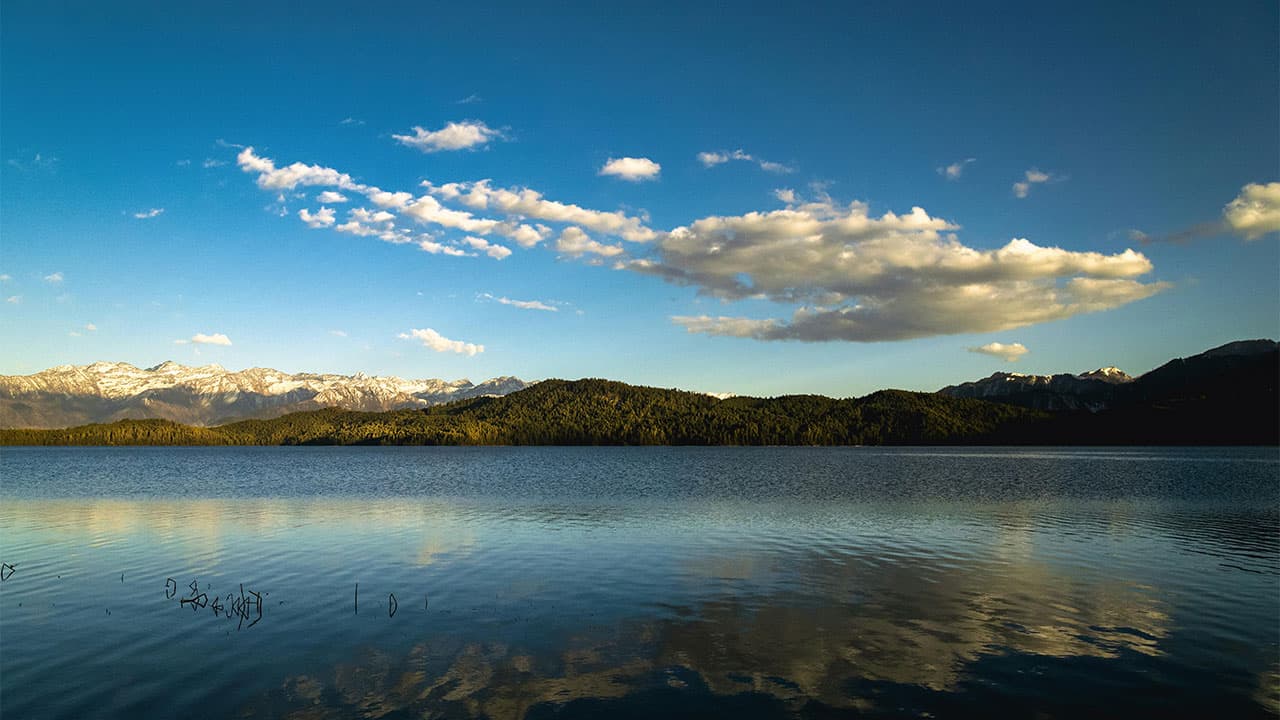 Rara Lake reflecting blue sky with snowy peaks in the distance.