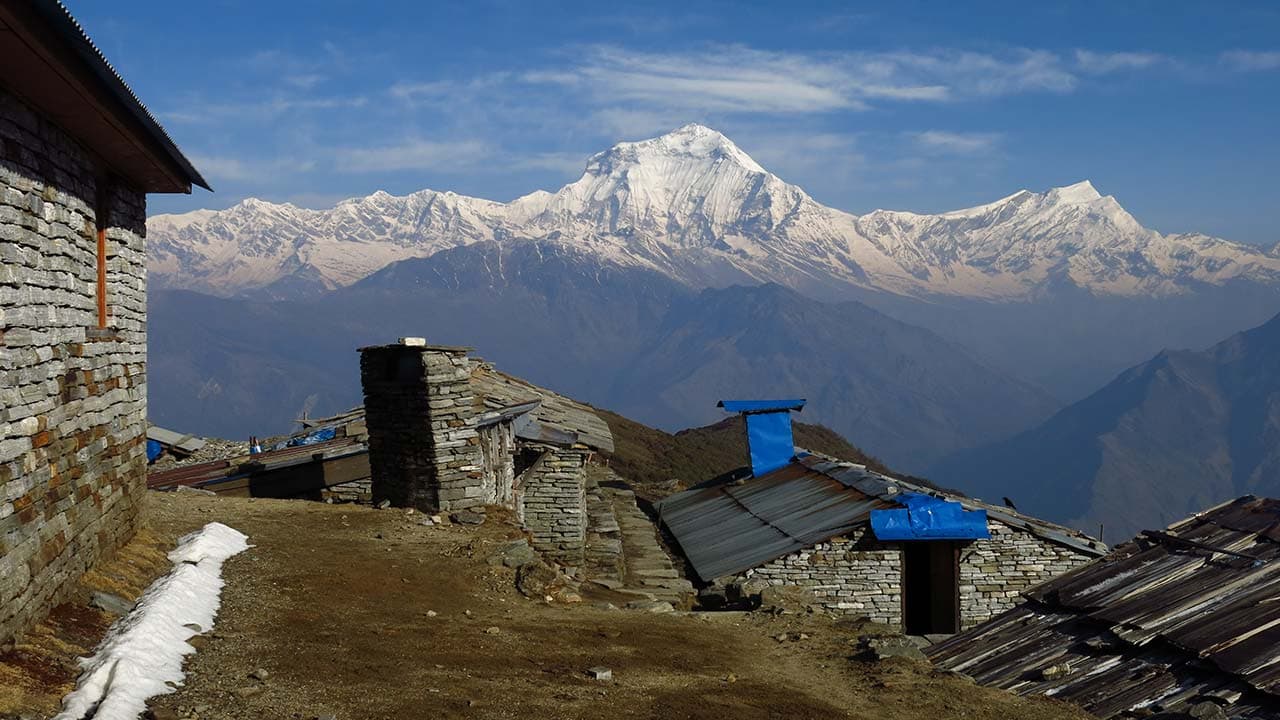 Stone teahouses and lodges on Khopra Danda with snow-capped Dhaulagiri mountain peaks in the background during the Khopra Ridge trek in Nepal.