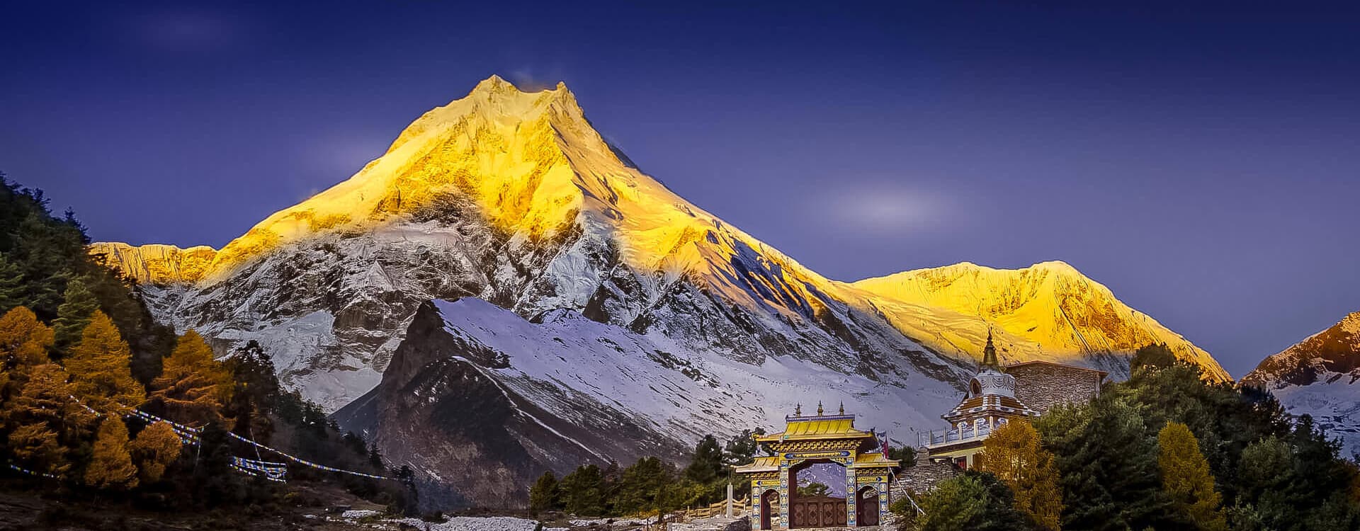 Golden sunrise illuminating Mount Manaslu and a traditional monastery gate in Lho Gaon during the 15 days Manaslu Circuit Trek.