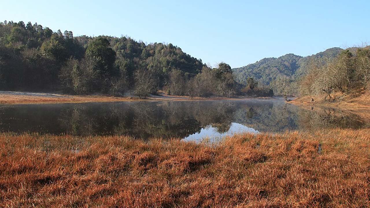 Calm water pond and reflection of green hills during the Kathmandu Valley Rim Trekking hike.