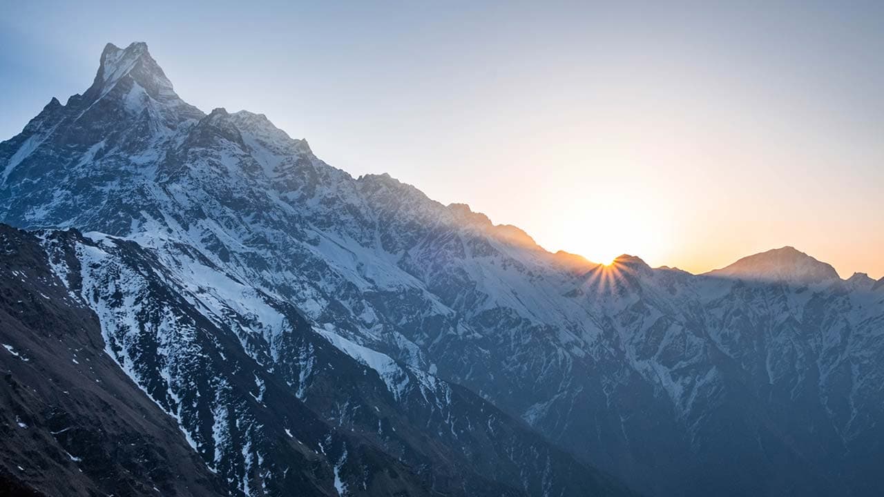 Sunrise glowing behind a snowy Himalayan mountain ridge next to Mount Machhapuchhre.