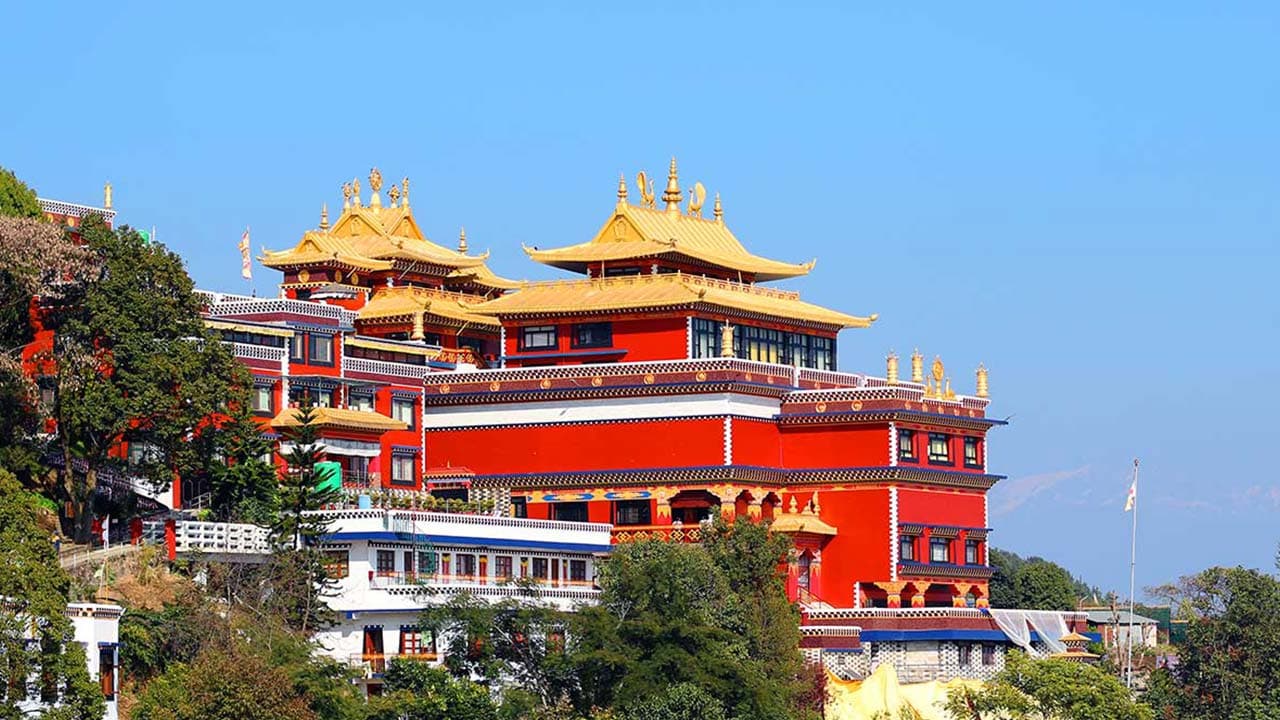 Red multi-tiered monastery building with golden roofs and surrounding greenery.