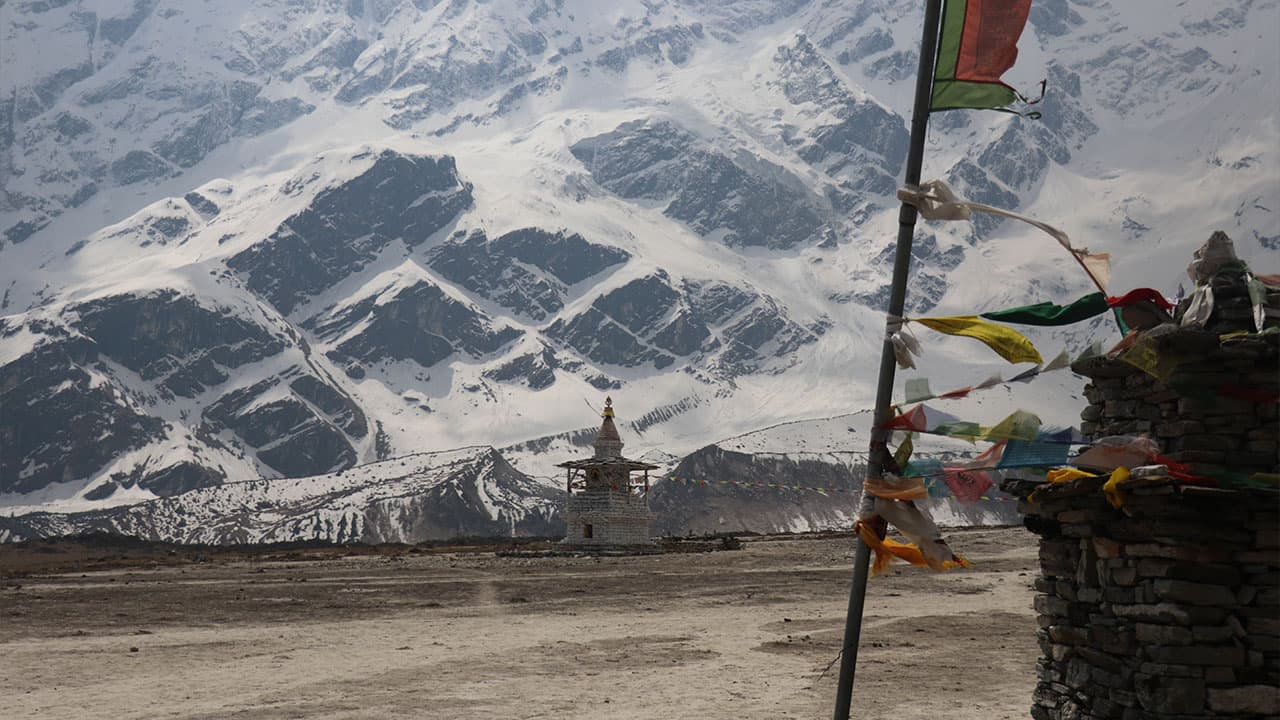 Traditional chorten and prayer flags against snowy Himalayan peaks during the 20 days Manaslu Circuit with Tsum Valley Trek.