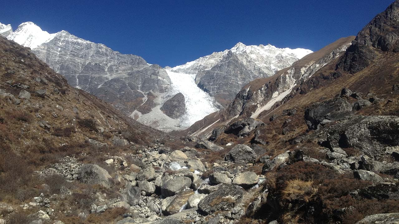 Rocky mountain valley leading up to a massive glacier flowing down between steep Himalayan peaks.