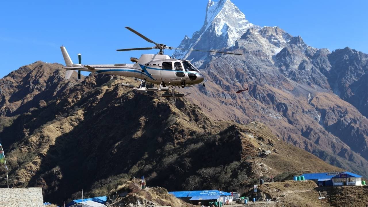 Silver and white helicopter flying over a mountain ridge.