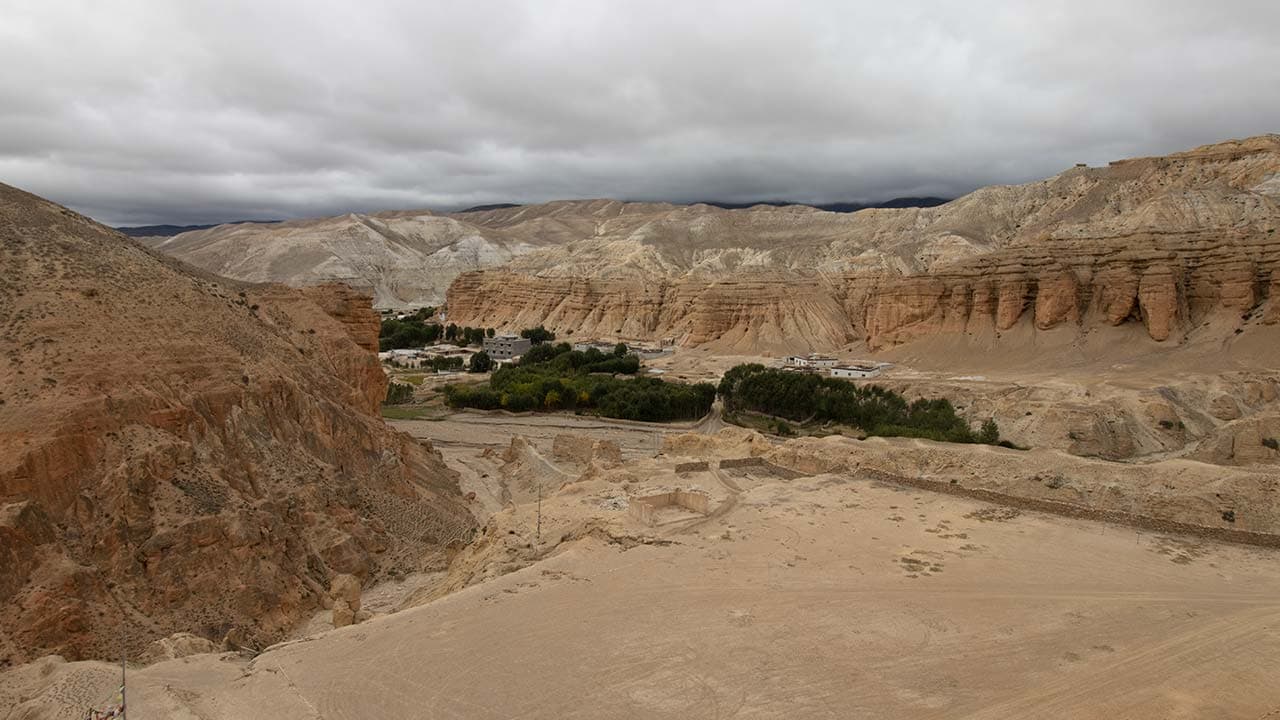 Green oasis village nestled within dramatic high-altitude desert canyons and eroded hills during the 13 Days Upper Mustang Trek.