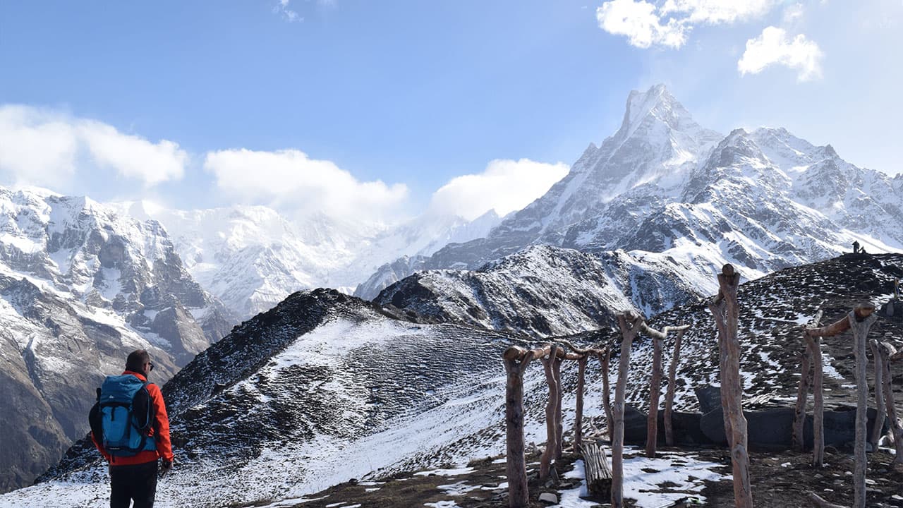 Trekker standing on a snowy ridge overlooking Machhapuchhre peak on the Mardi Himal trek.